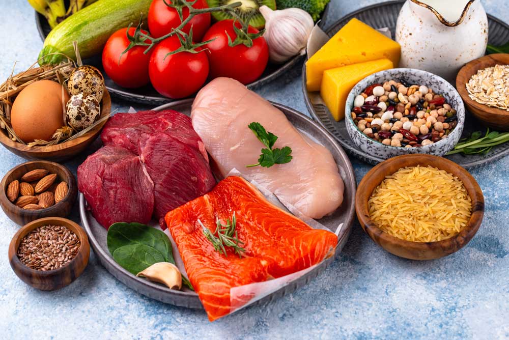 Assortment of high-protein whole foods including salmon, chicken, beef, eggs, nuts, legumes, and vegetables for a balanced diet.
